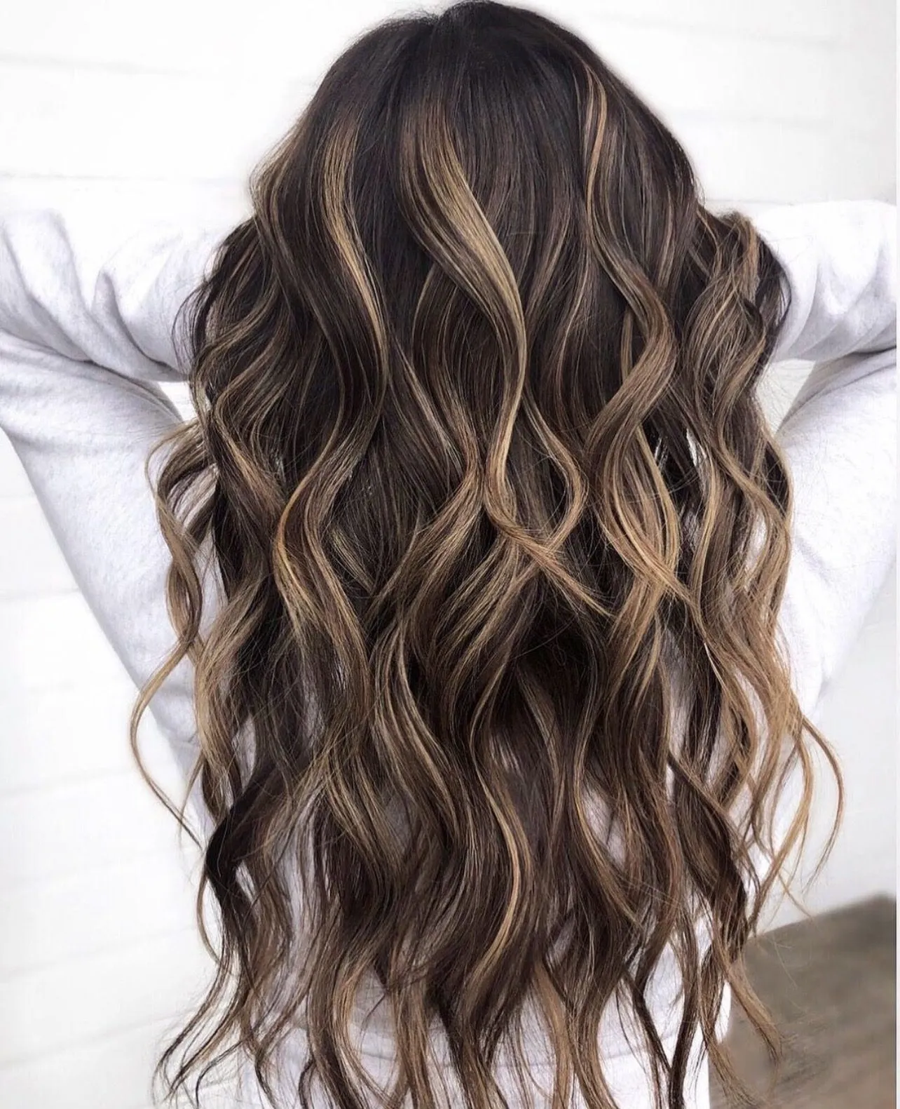 Long brunette hair with soft caramel balayage, styled in loose waves